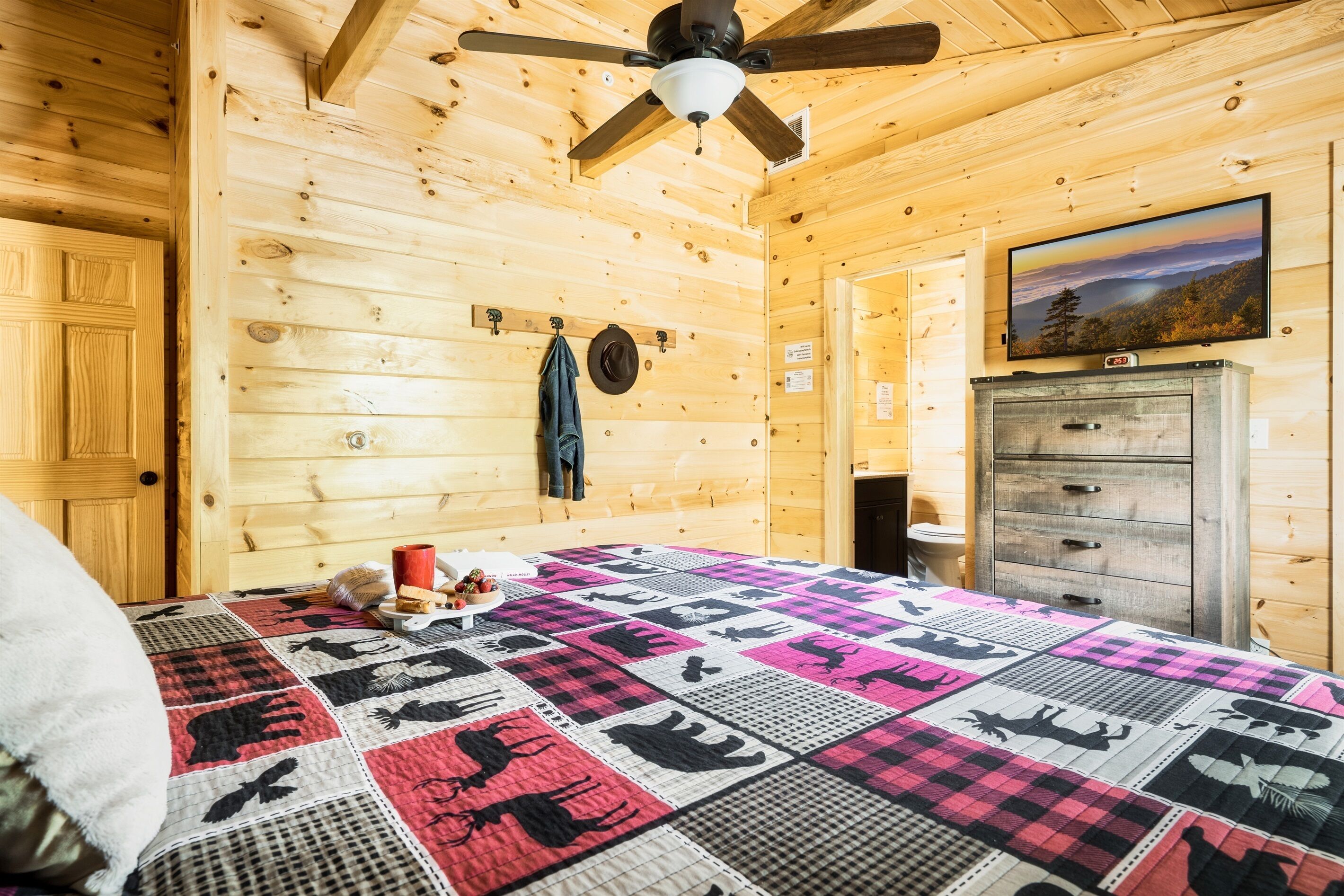 Une chambre dans un chalet en bois, équipée d’un lit, d’un ventilateur de plafond, d’une télévision et d’une commode.