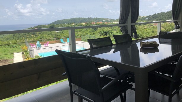 A balcony with a table and chairs, overlooking a swimming pool and lush greenery.