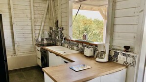 A compact kitchen with a wooden countertop, white cabinets, a window with a view, and a tiled backsplash.