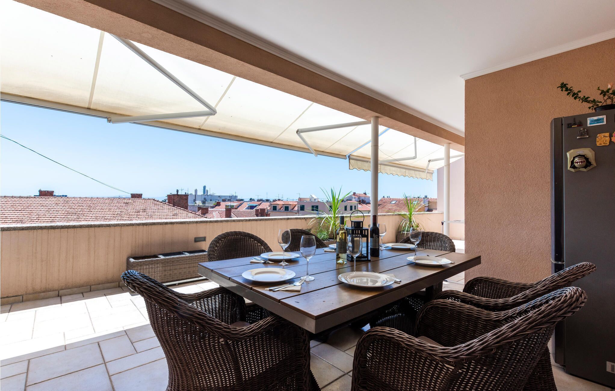 A terrace with a table set for dining, wicker chairs, and a view of the cityscape.