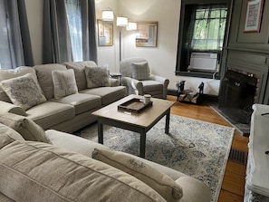 A living room with a sofa, armchair, and coffee table. There is a fireplace and a rug on the floor.