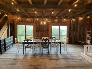 A rustic dining area with a wooden table and chairs, large windows, and a staircase.
