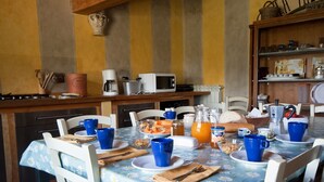 Een eettafel gedekt met blauwe bekers, borden en een karaf sinaasappelsap, omringd door witte stoelen.