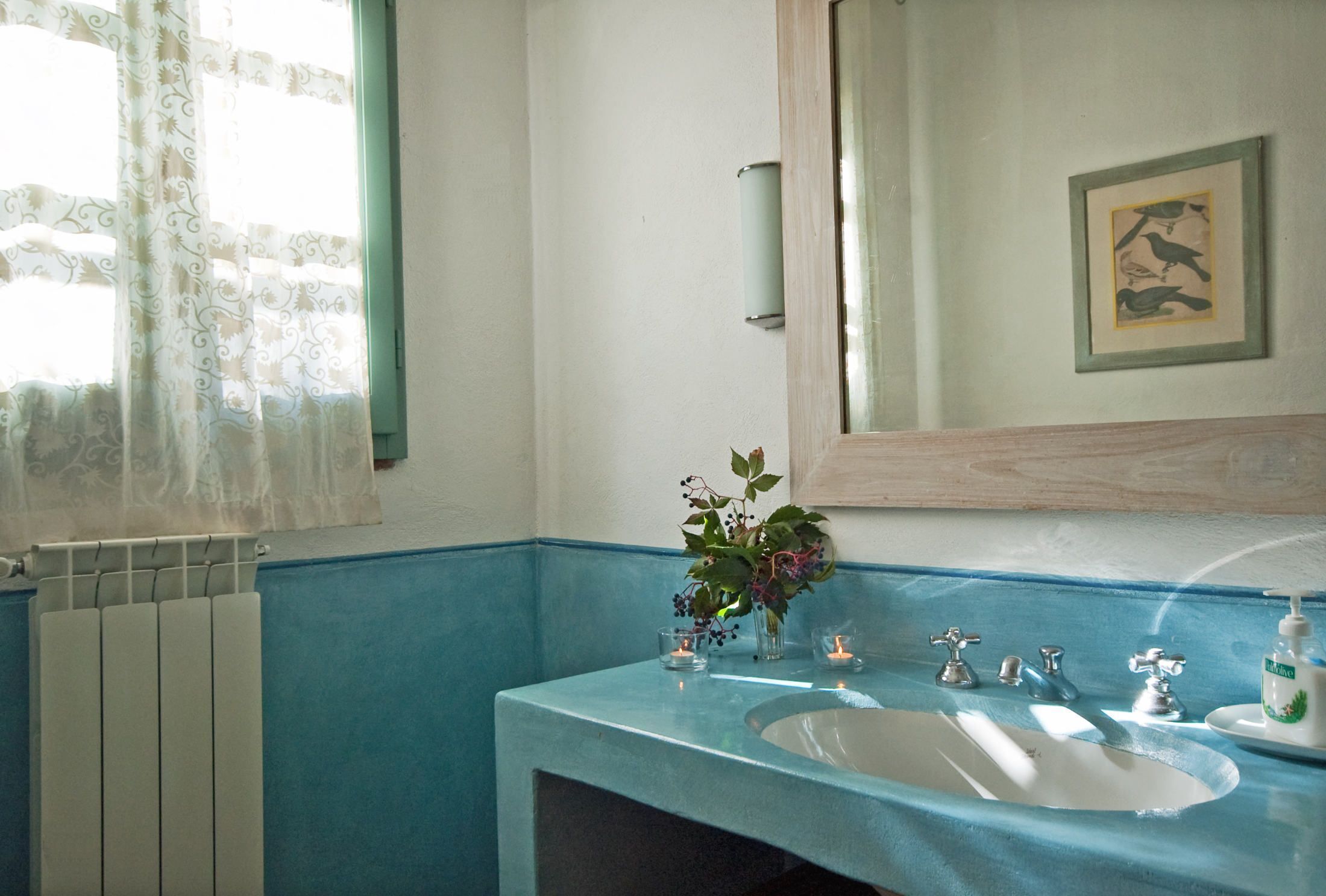 Ein Badezimmer mit blauem Waschbecken, einem Spiegel, einer Heizung und einem Fenster mit Vorhängen.