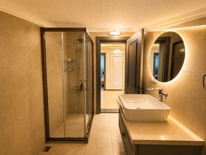 Un baño moderno con ducha de vidrio, un espejo grande y un lavamanos blanco.