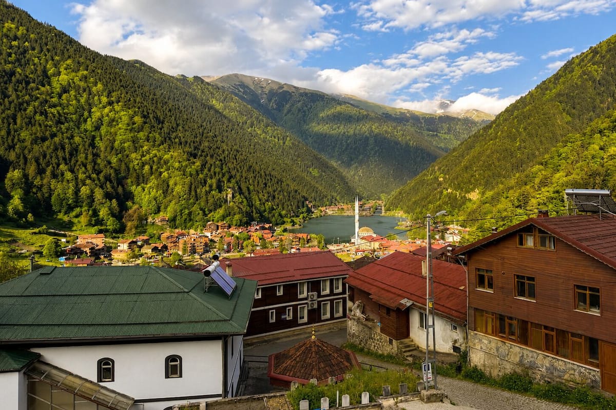 A mountainous village with traditional buildings, a mosque, and a lake.