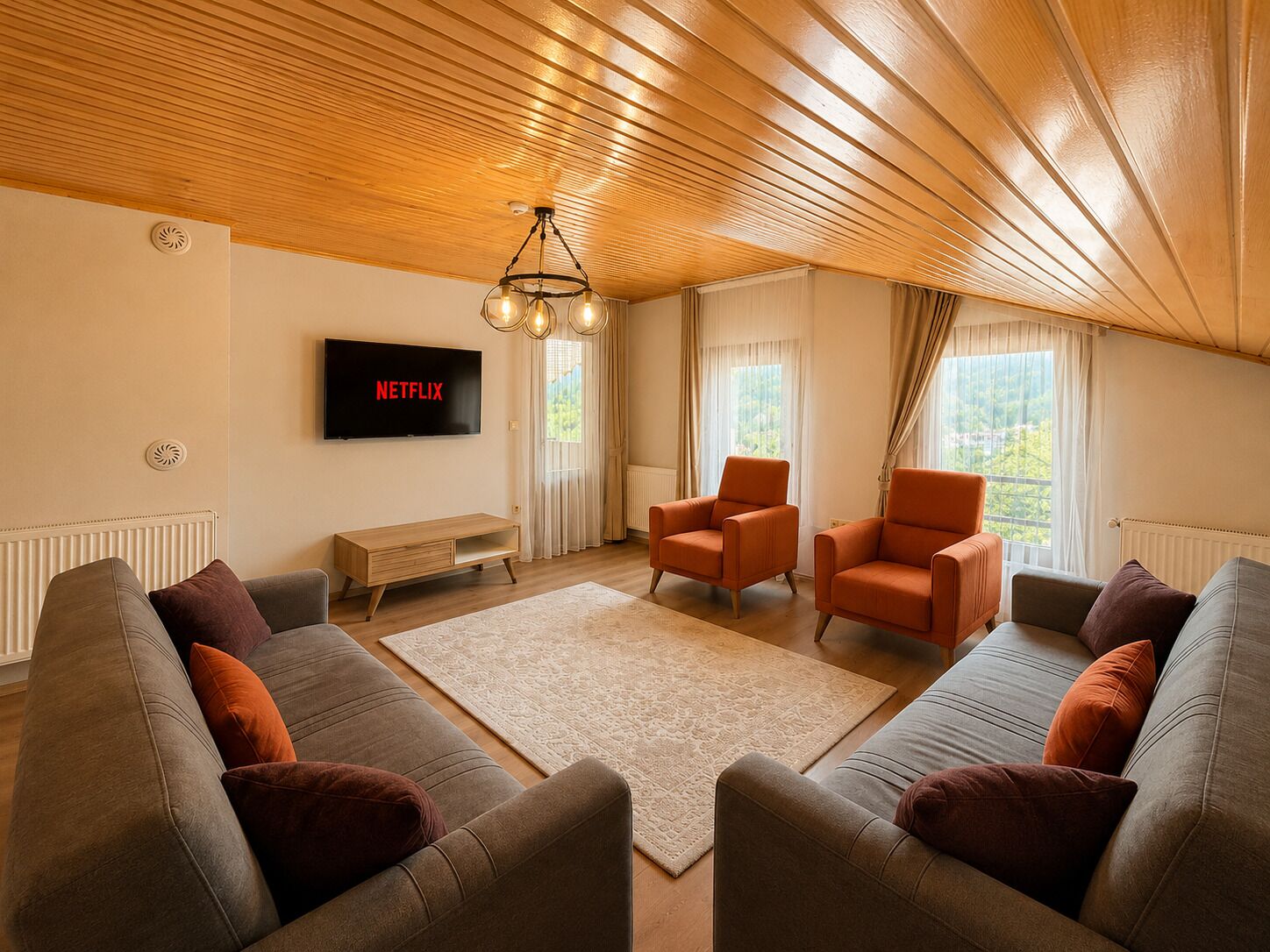 Una sala de estar con techo de madera, un televisor montado en la pared, dos sillones, un sofá y una pequeña mesa de centro.