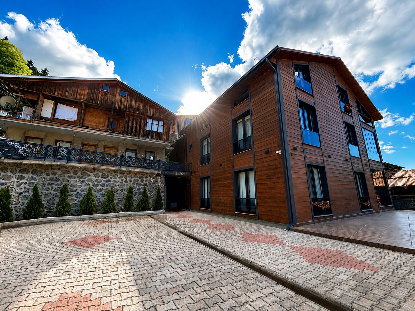 A modern building with a stone facade and wooden upper levels, featuring a paved courtyard.