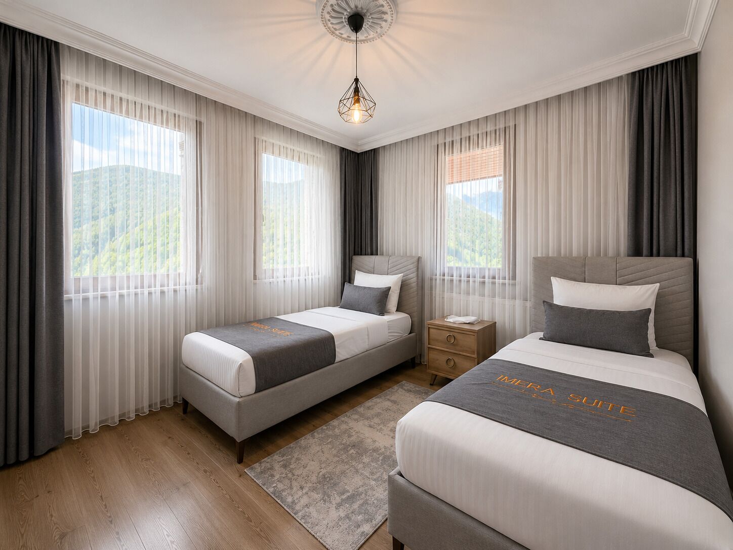 Una camera d'albergo con due letti, un comodino, un lampadario a soffitto e ampie finestre con tende.