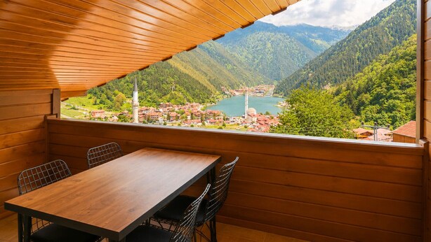 A wooden-paneled room with a table and chairs, a large window offering a view of a lake and mountains.