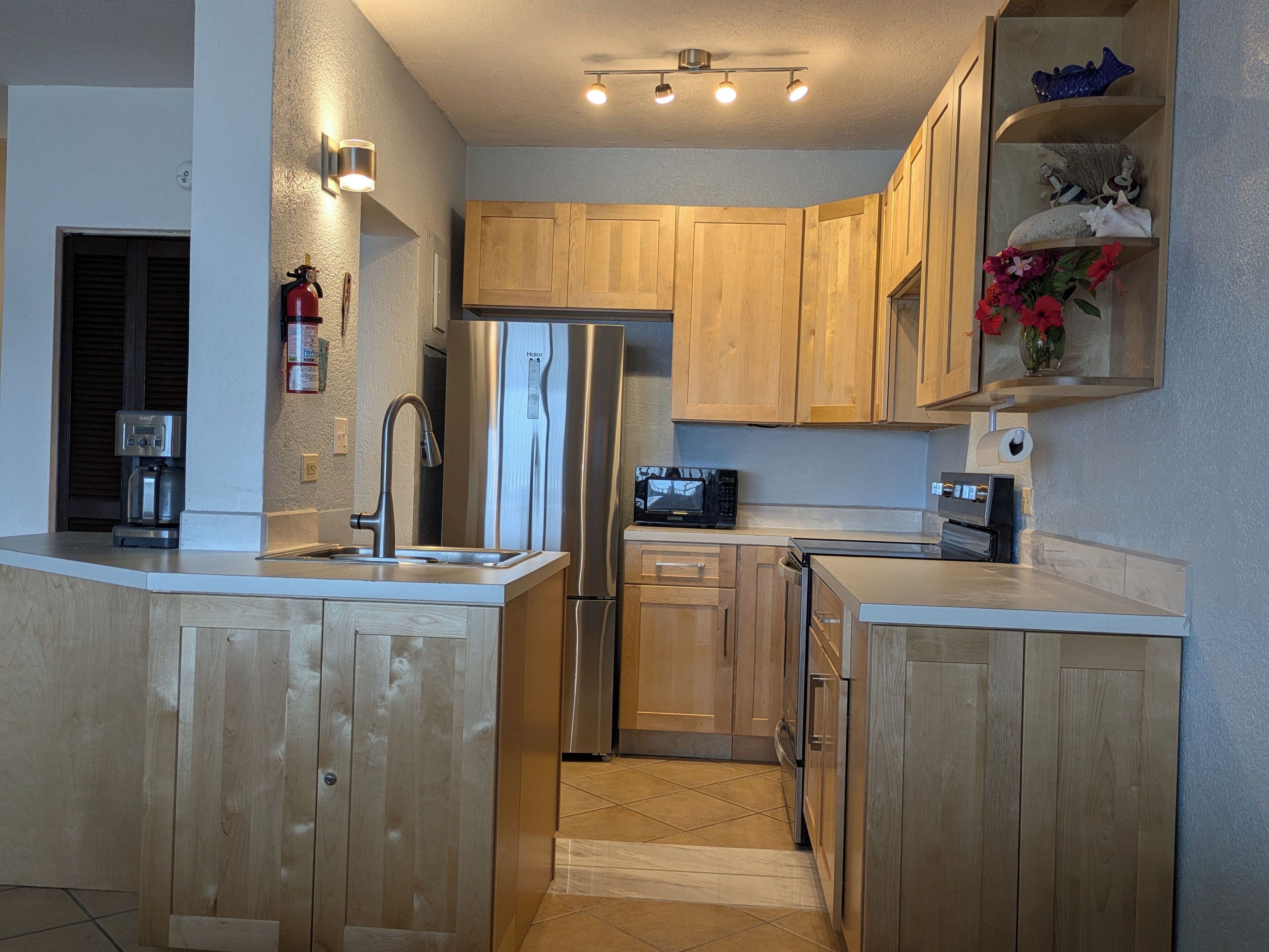 A compact kitchen with wooden cabinets, a stainless steel refrigerator, a microwave, and a coffee maker.