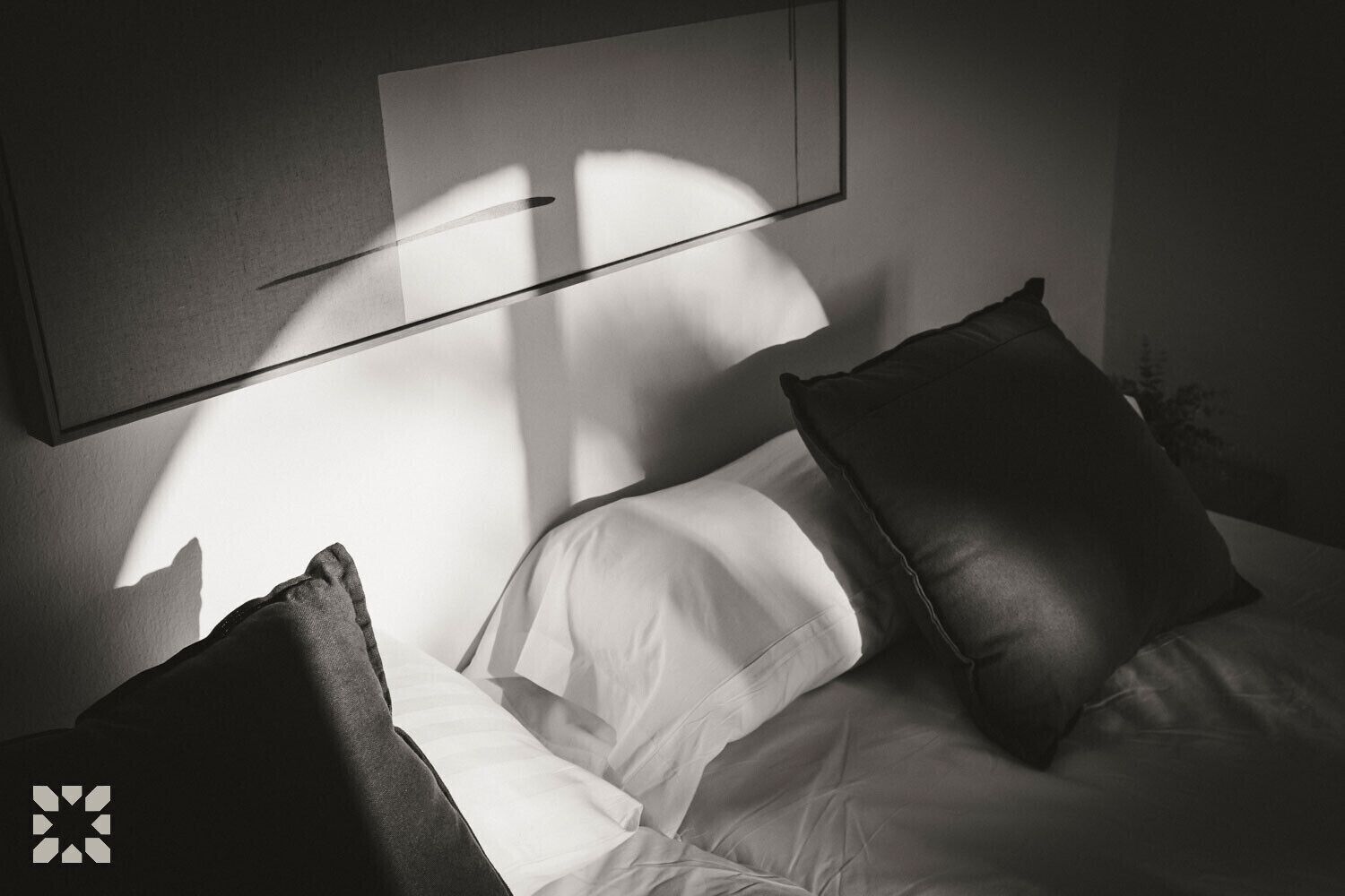 A bedroom with a bed, pillows, and a wall-mounted light fixture casting shadows.