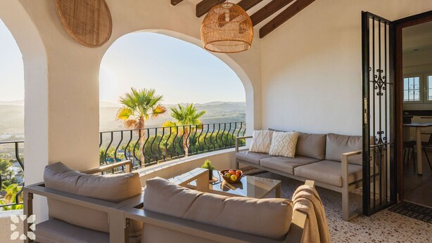 Ein Balkon mit einer Sitzecke, einem Tisch mit Obst und Blick auf Palmen und Berge.