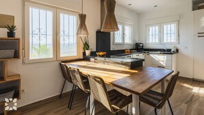 Eine moderne Küche mit Holztisch, Korbstühlen, Pendelleuchten und großen Fenstern.