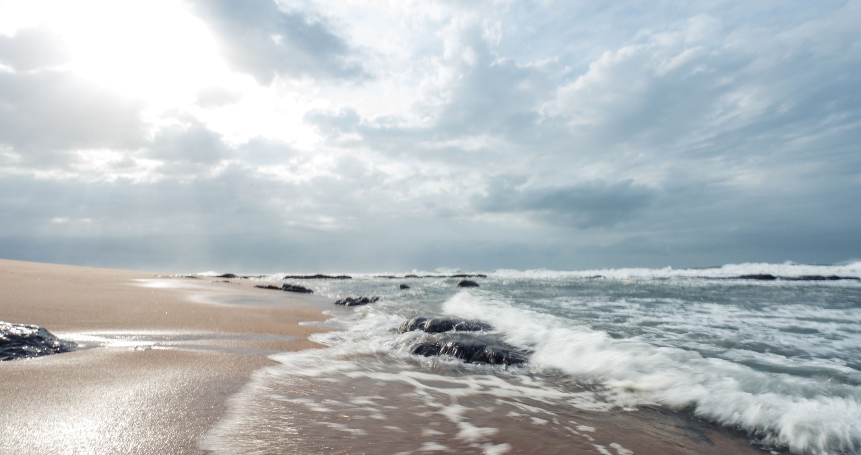 Une plage où les vagues se brisent sur le rivage sous un ciel nuageux.