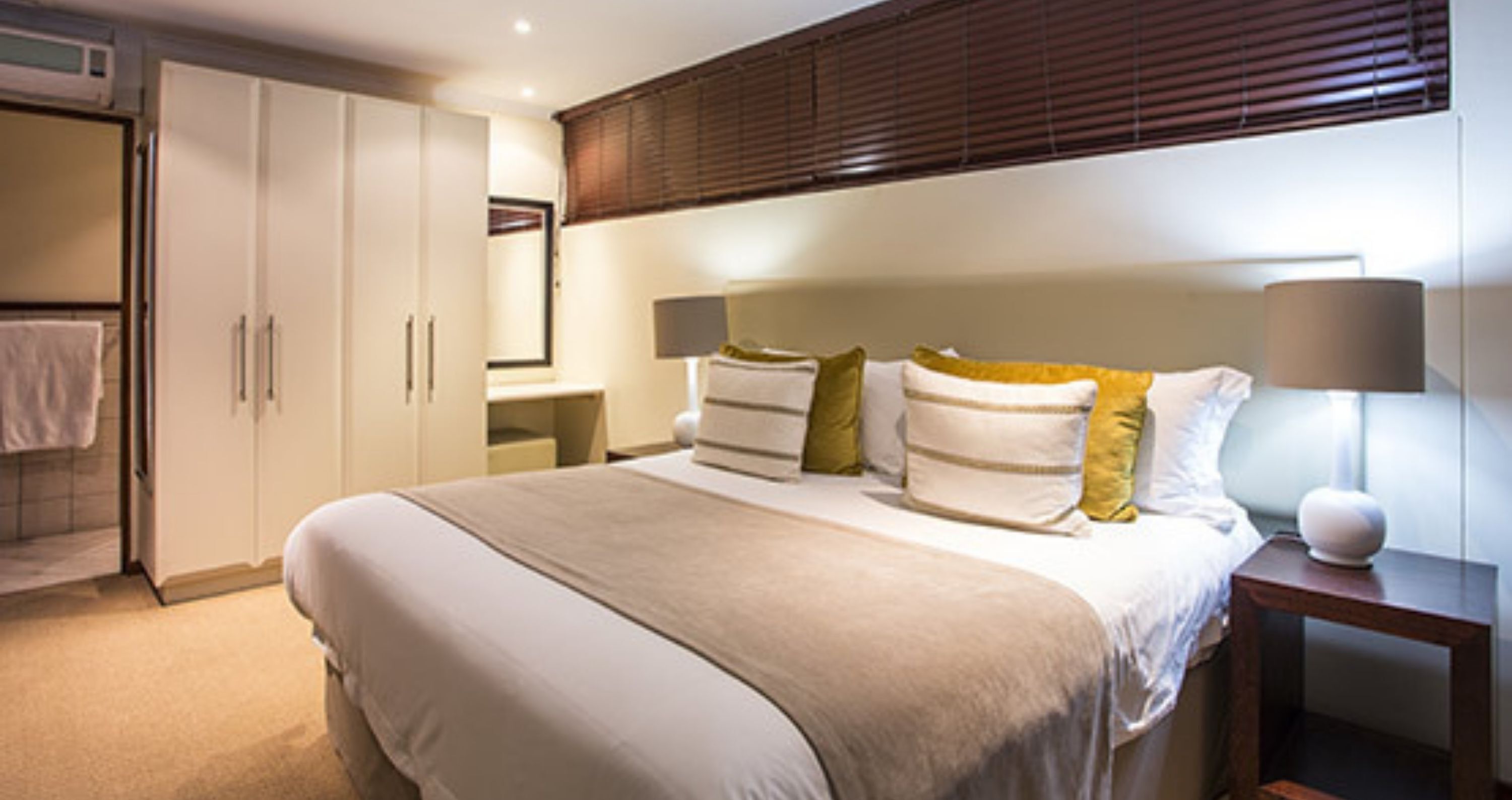 A bedroom with a large bed, bedside lamps, a wardrobe, and a mirror.