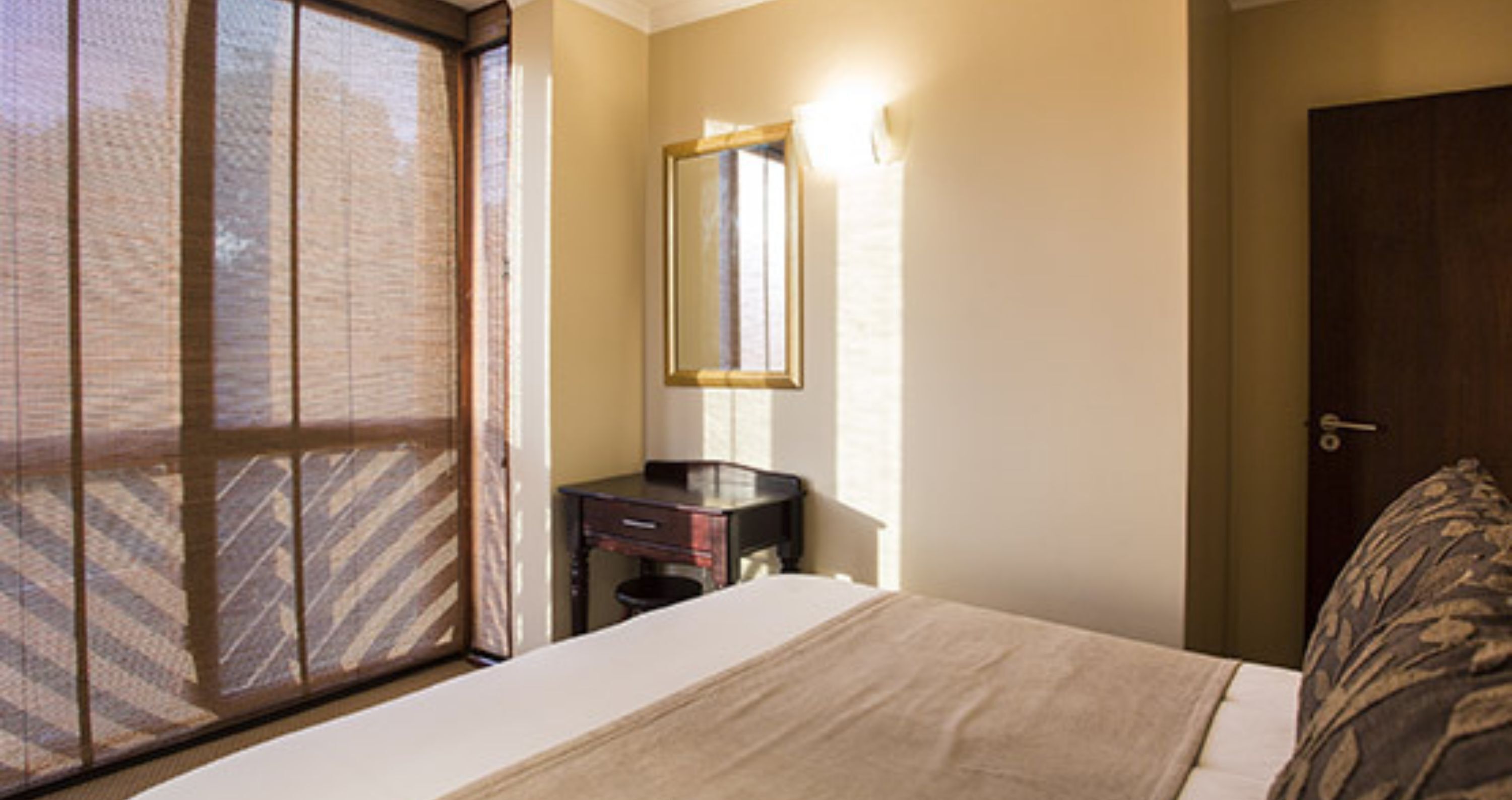 A hotel room with a bed, a small bedside table, a mirror, and a door.