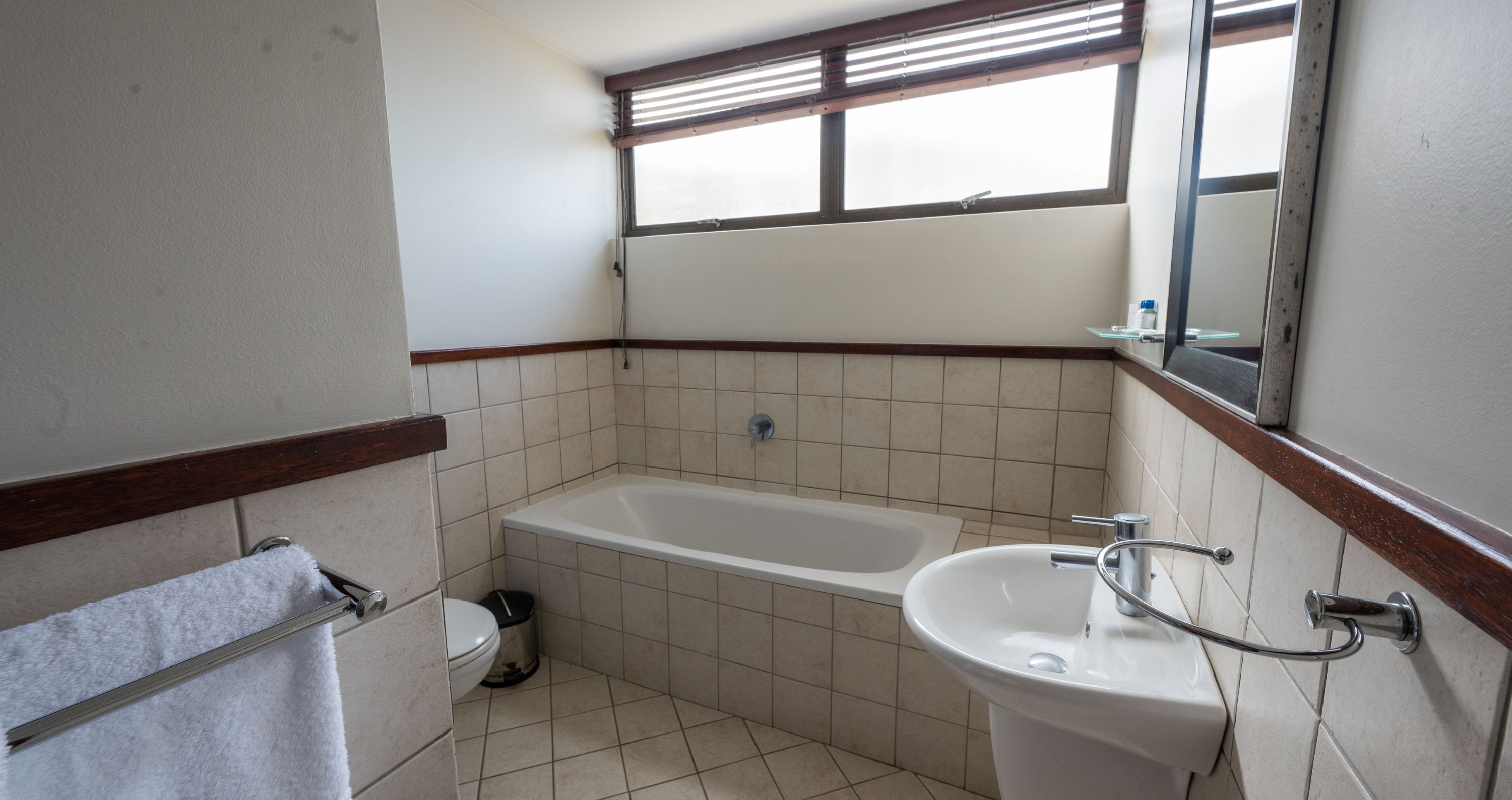 Ein Badezimmer mit Badewanne, Waschbecken, Toilette und einem Fenster mit Jalousien.