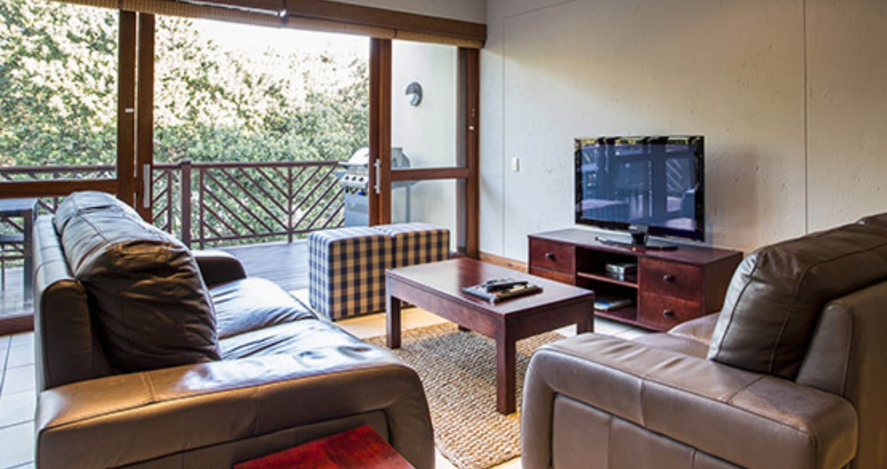 A living room with leather sofas, a wooden coffee table, and a television on a stand.