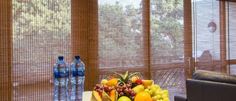 Una mesa con una bandeja de frutas y dos botellas de agua frente a una ventana con vista a árboles.
