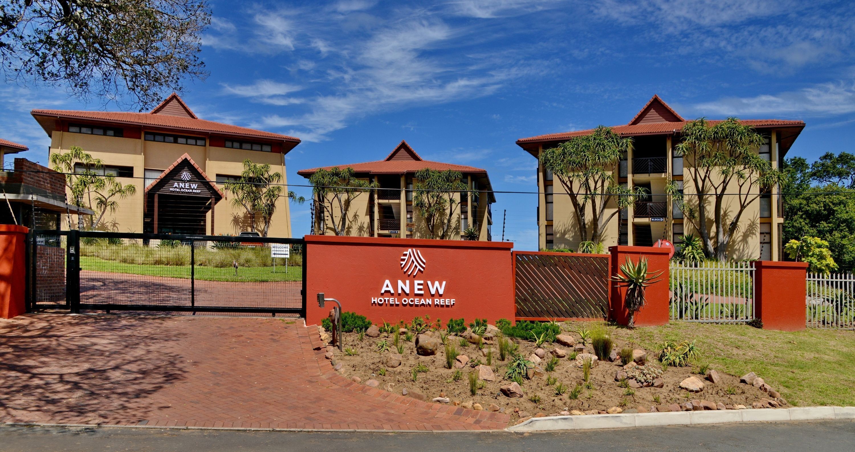 L'entrée de l'hôtel ANEW Ocean Reef, avec sa porte rouge, ses palmiers et un ciel d'un bleu éclatant.