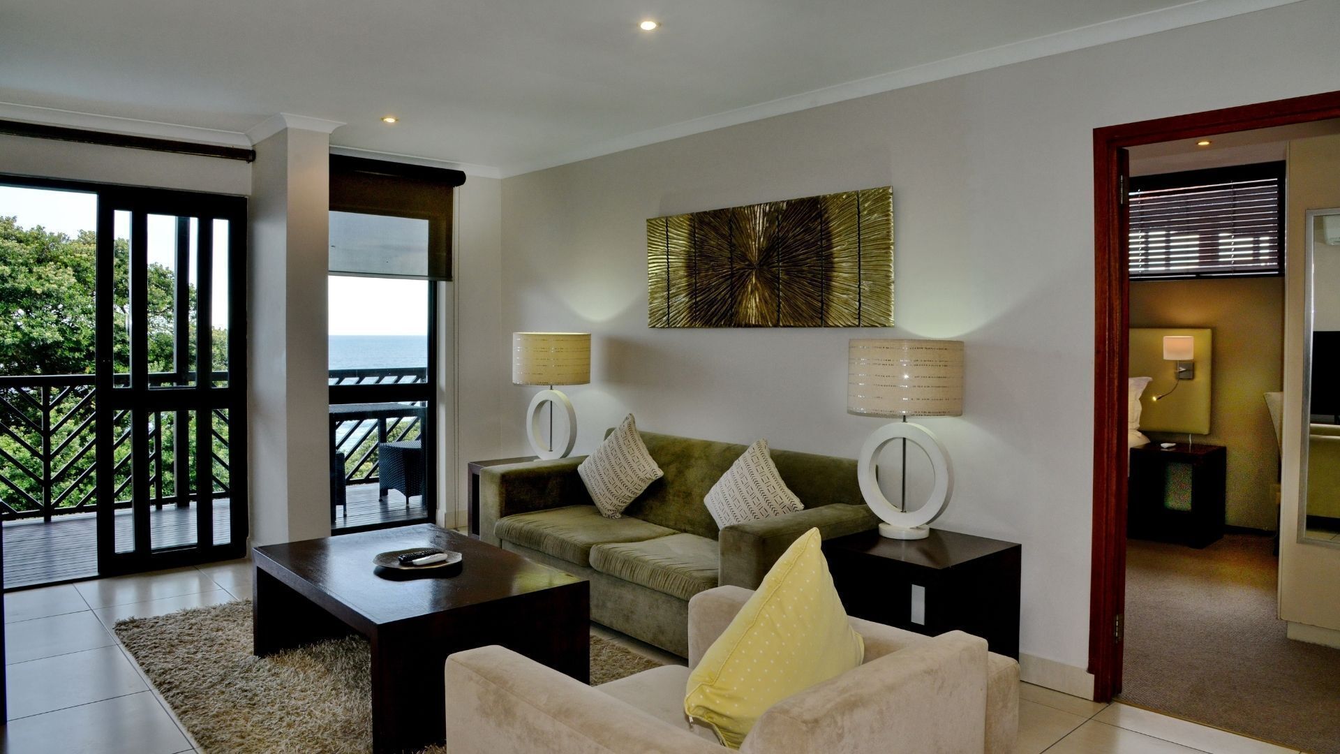 A modern living room with a sofa, two side tables with lamps, a coffee table, and a large window with a view of the outdoors.