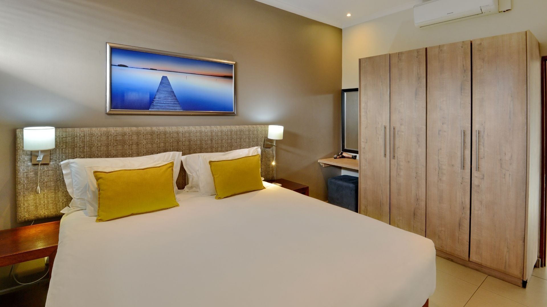 Habitación de hotel con una cama grande, dos lámparas de noche, un armario de madera y un televisor montado en la pared.