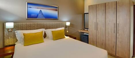 Habitación de hotel con una cama grande, dos lámparas de noche, un armario de madera y un televisor montado en la pared.