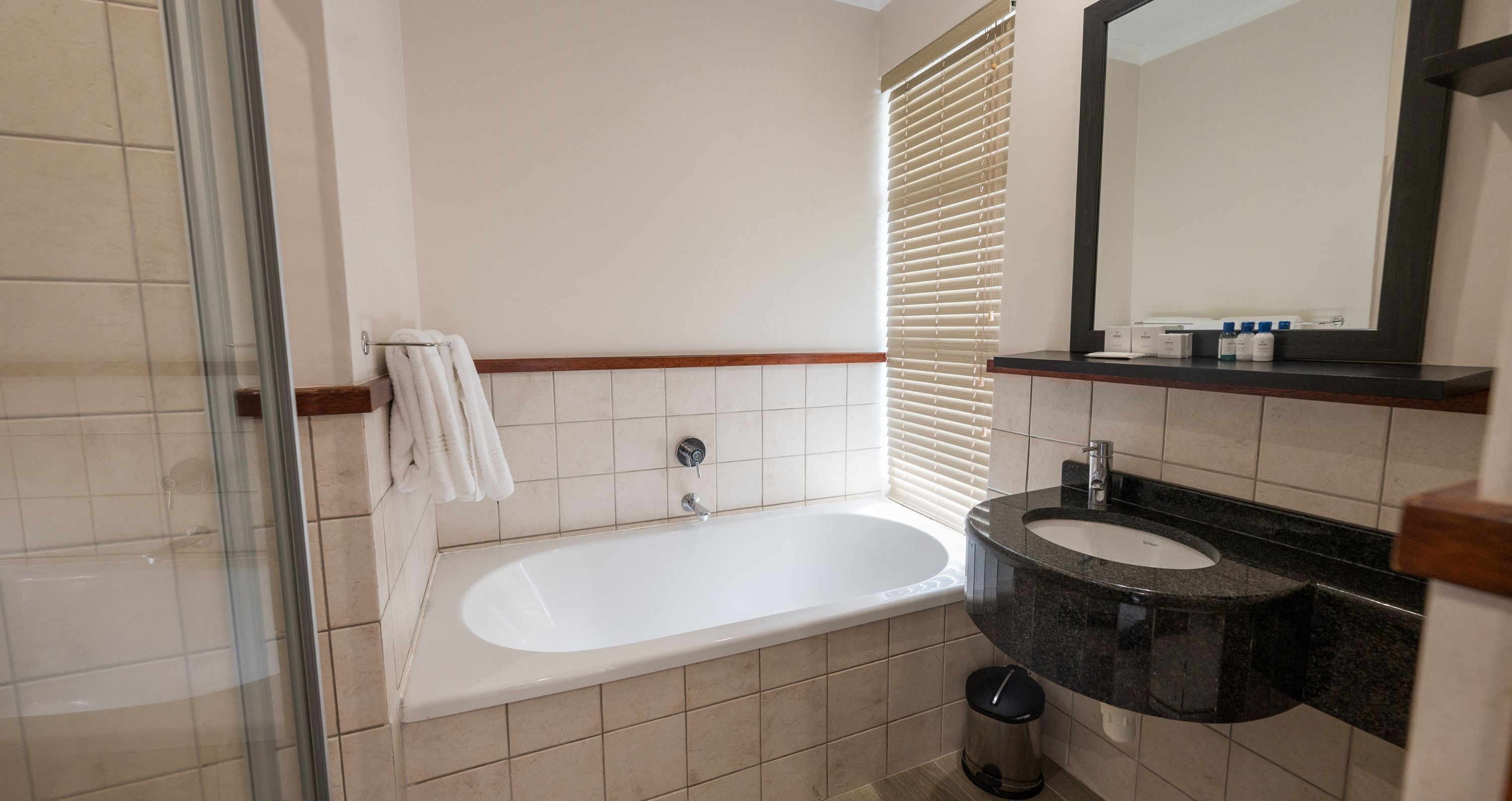 A bathroom with a bathtub, a sink, a mirror, and a window with blinds.