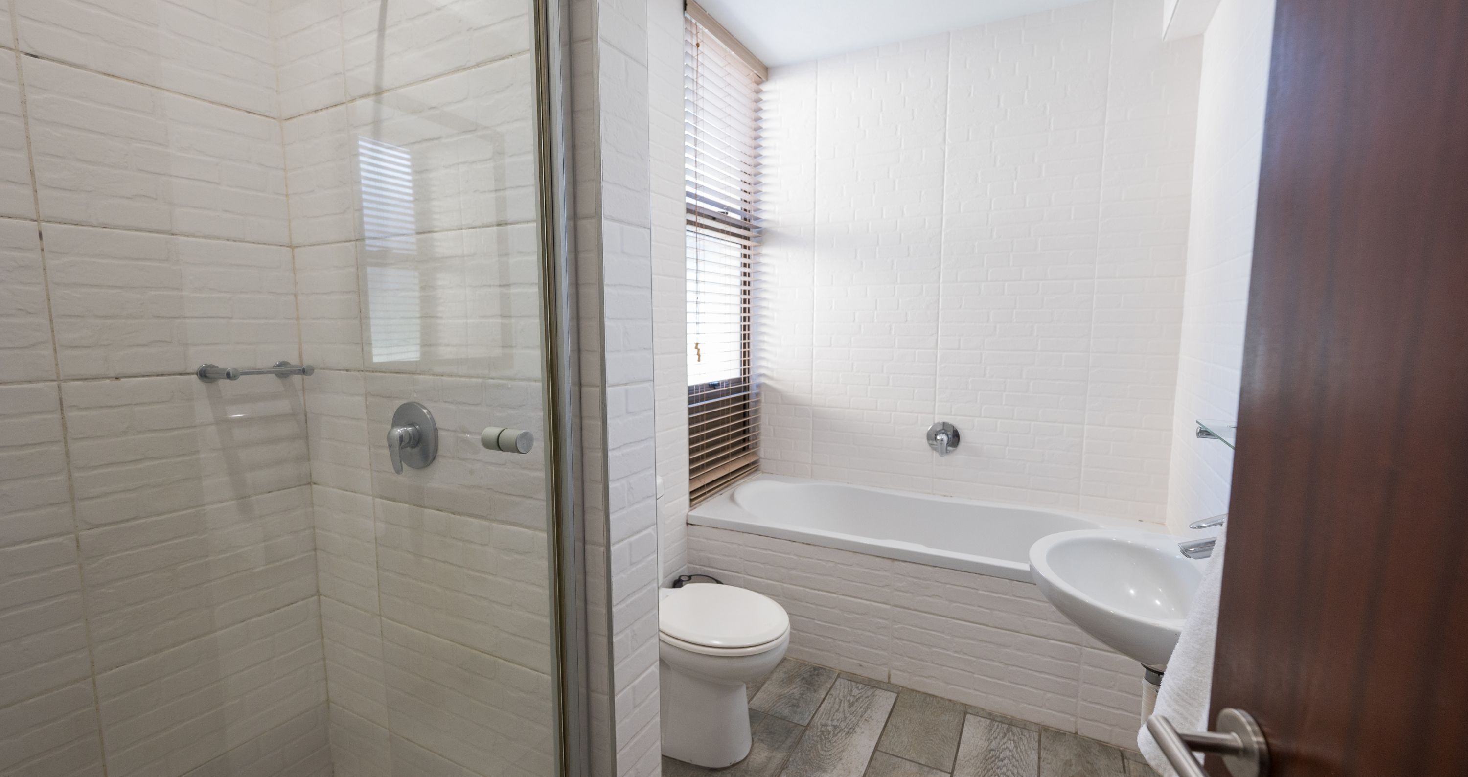 Un baño con azulejos blancos tipo metro, cerramiento de ducha de vidrio, inodoro blanco y bañera blanca con lavamanos.