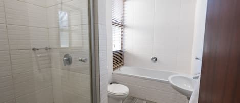 Un baño con azulejos blancos tipo metro, cerramiento de ducha de vidrio, inodoro blanco y bañera blanca con lavamanos.