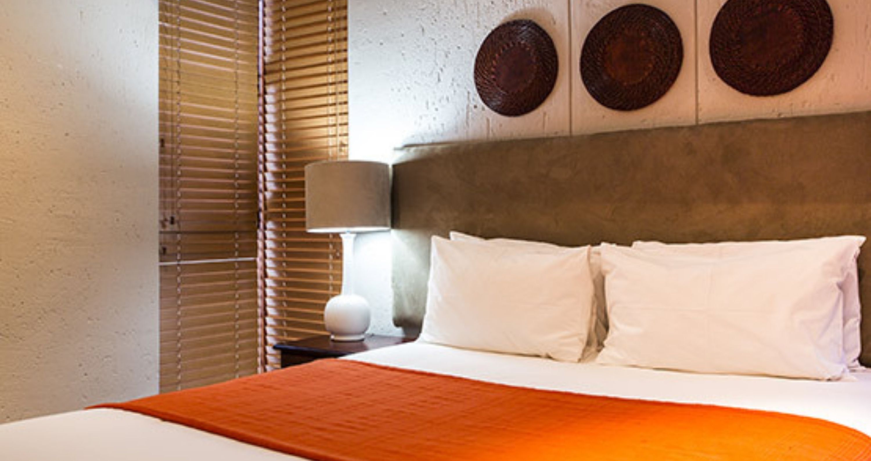 Une chambre d’hôtel avec un lit, une table de chevet, une lampe et un mur orné de trois motifs circulaires.
