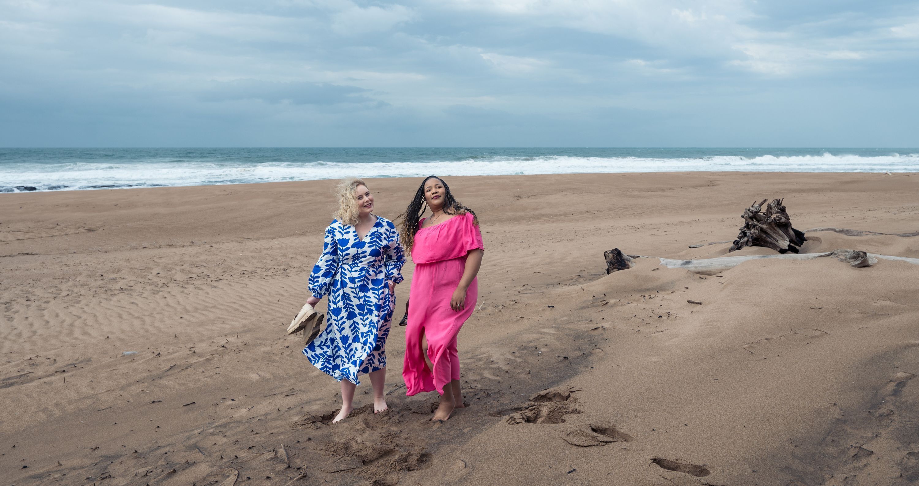 Deux personnes se tiennent sur une plage de sable, avec l’océan et ses vagues en arrière-plan.