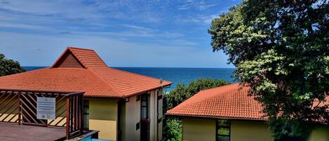 A resort with a swimming pool, a view of the sea, and a building with a red-tiled roof.