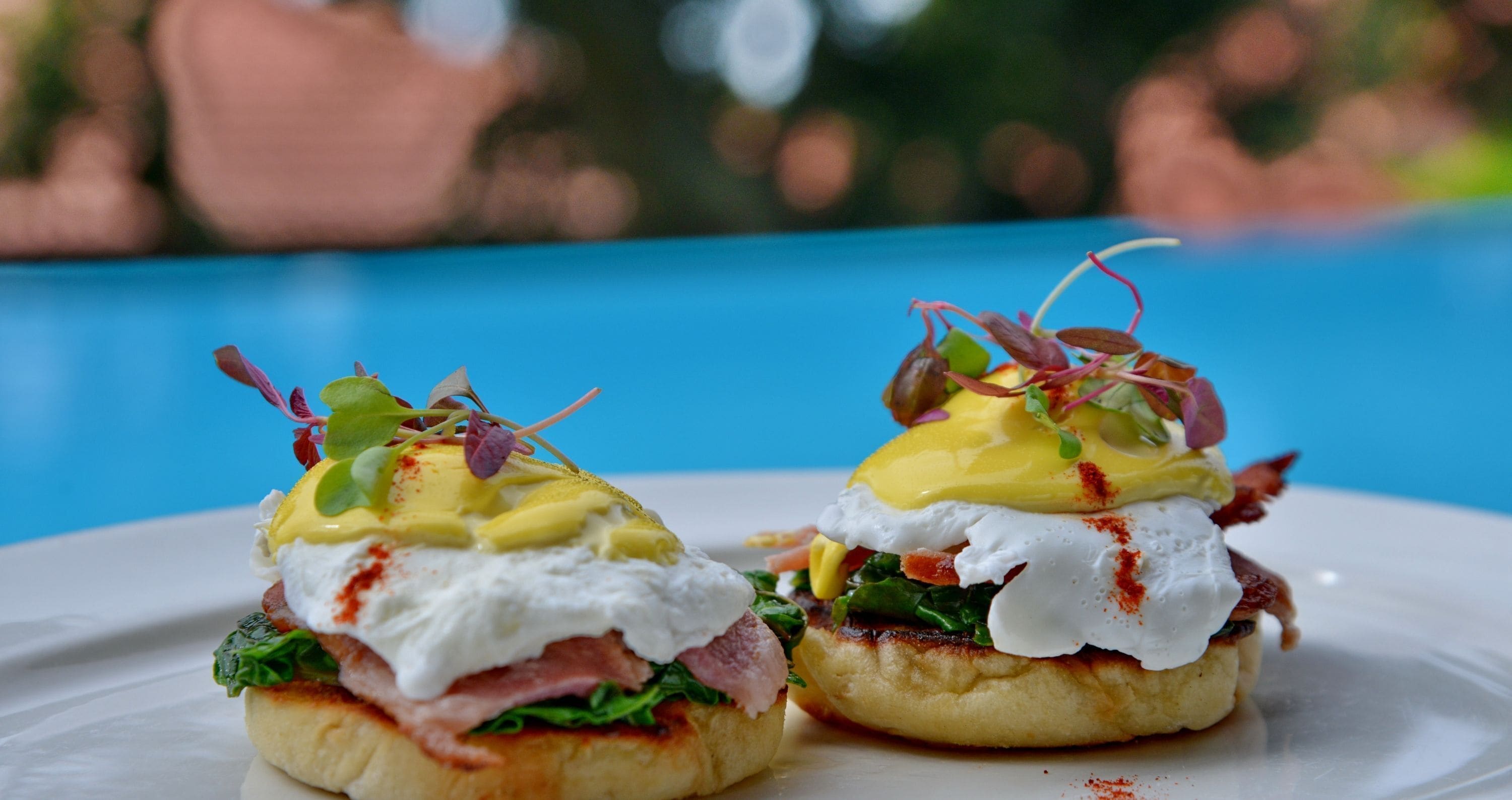 Two eggs benedict sandwiches on a white plate with a blue background.