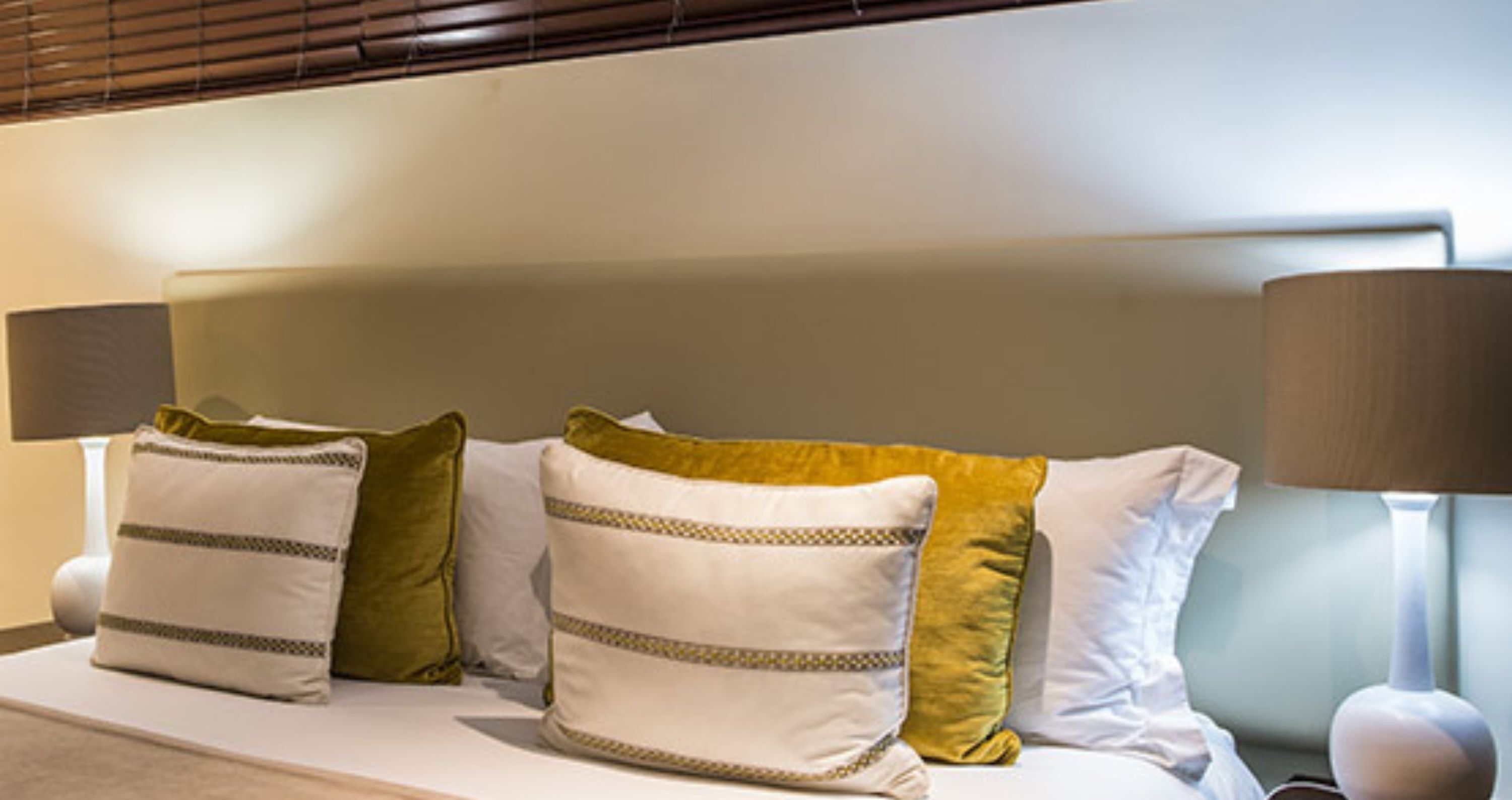 A neatly made bed with a headboard, multiple pillows, and two bedside lamps.
