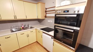 Una cocina con gabinetes amarillo claro, un horno negro y un lavamanos de acero inoxidable.