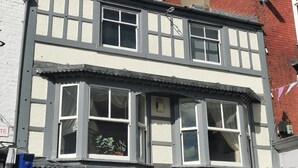 Un edificio de dos plantas con fachada blanca y varias ventanas, incluidas ventanas salientes con cortinas.