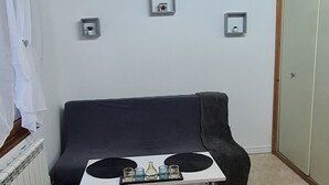 A cozy living room with a dark sofa, a white coffee table, and a black furry rug. There are three small picture frames on the wall and a radiator on the left. - Magnifique Studio de 20m2 Pour 1 à 4 Personnes (Les Rousses)