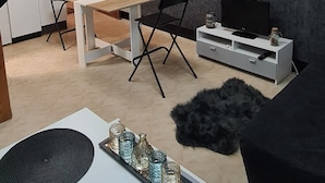 A modern living room with a wooden ceiling, a dining area with a table and chairs, a TV on a white cabinet, and a black sofa. - Magnifique Studio de 20m2 Pour 1 à 4 Personnes (Les Rousses)