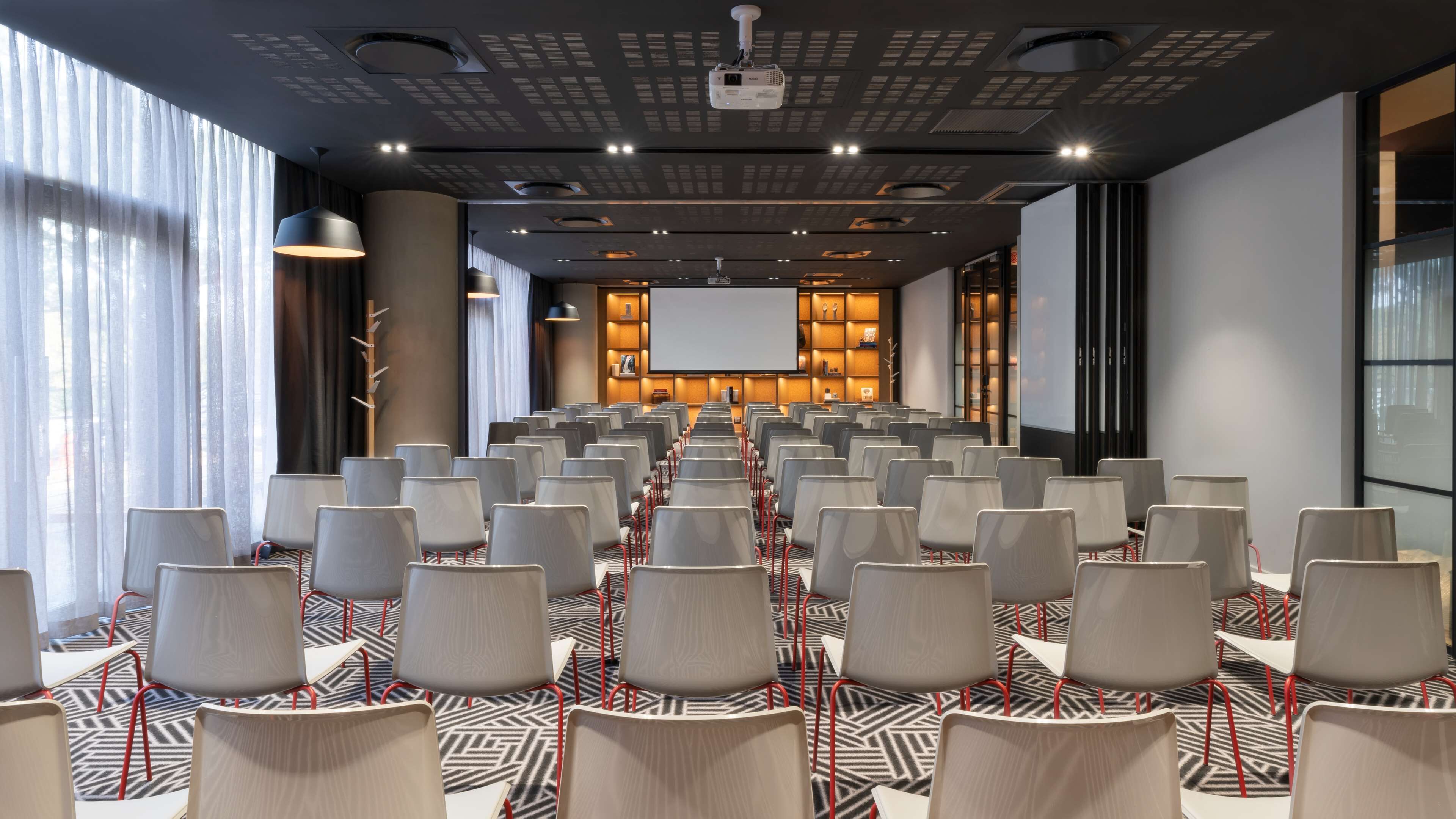 Un salón de conferencias con filas de sillas, una pantalla grande y una alfombra estampada.