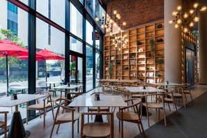 Un caffè moderno con ampie finestre, tavoli in legno e una parete in mattoni con scaffali.