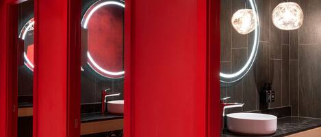 A modern bathroom with red walls, dark tiled floors, and circular mirrors with illuminated edges.
