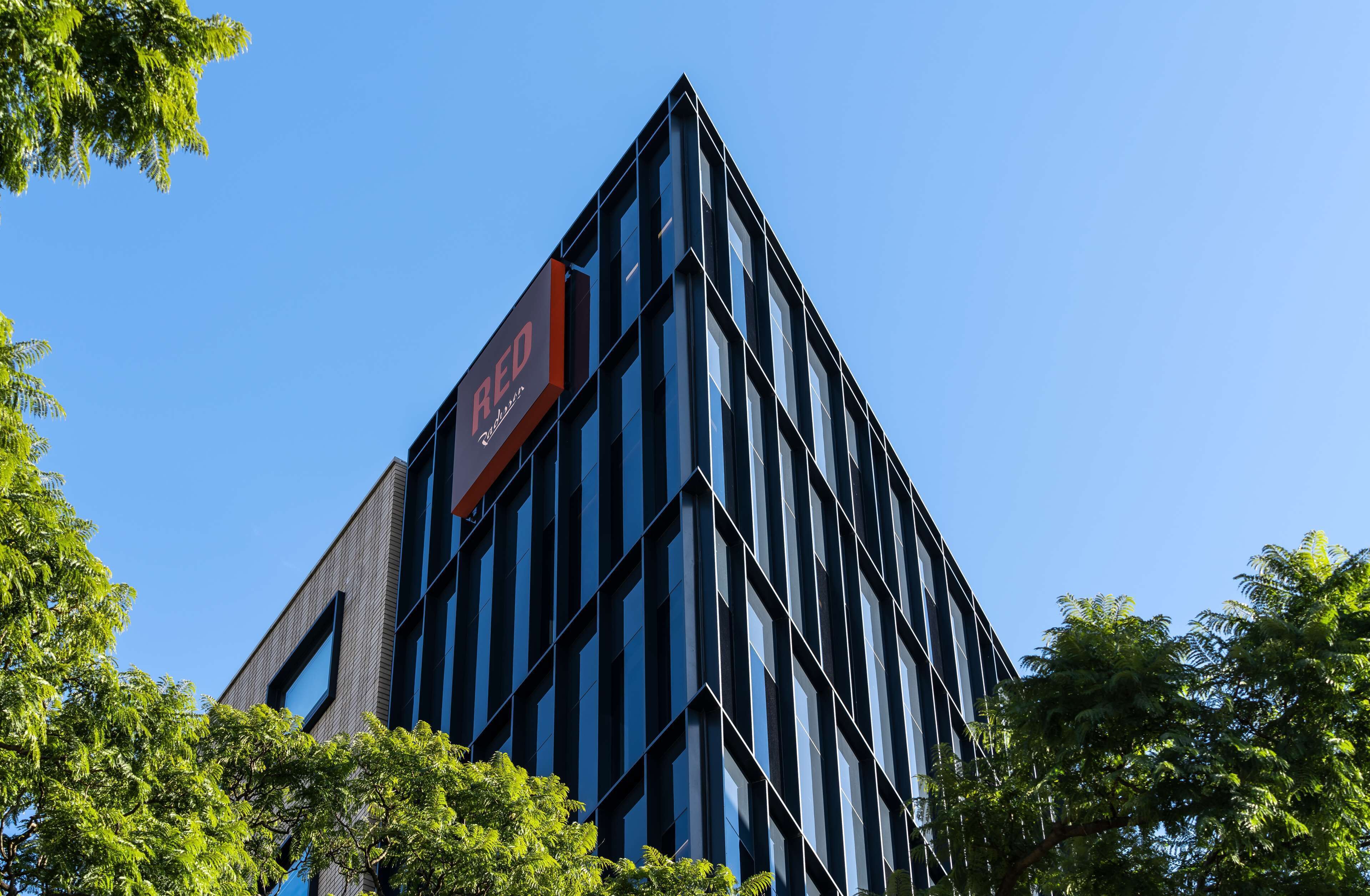 Un edificio moderno con un llamativo letrero 'RED', rodeado de árboles.
