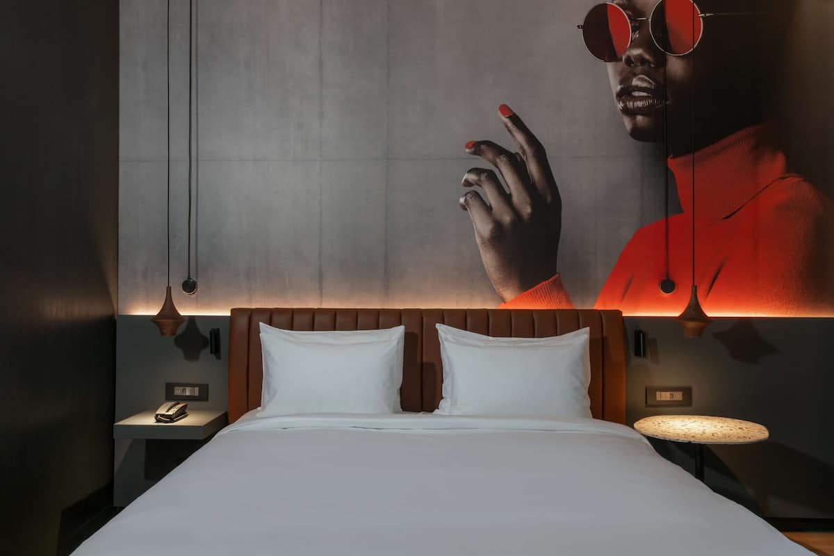 Una habitación de hotel moderna con una cama grande, una mesita de noche, una lámpara de pared y un cartel grande en la pared.