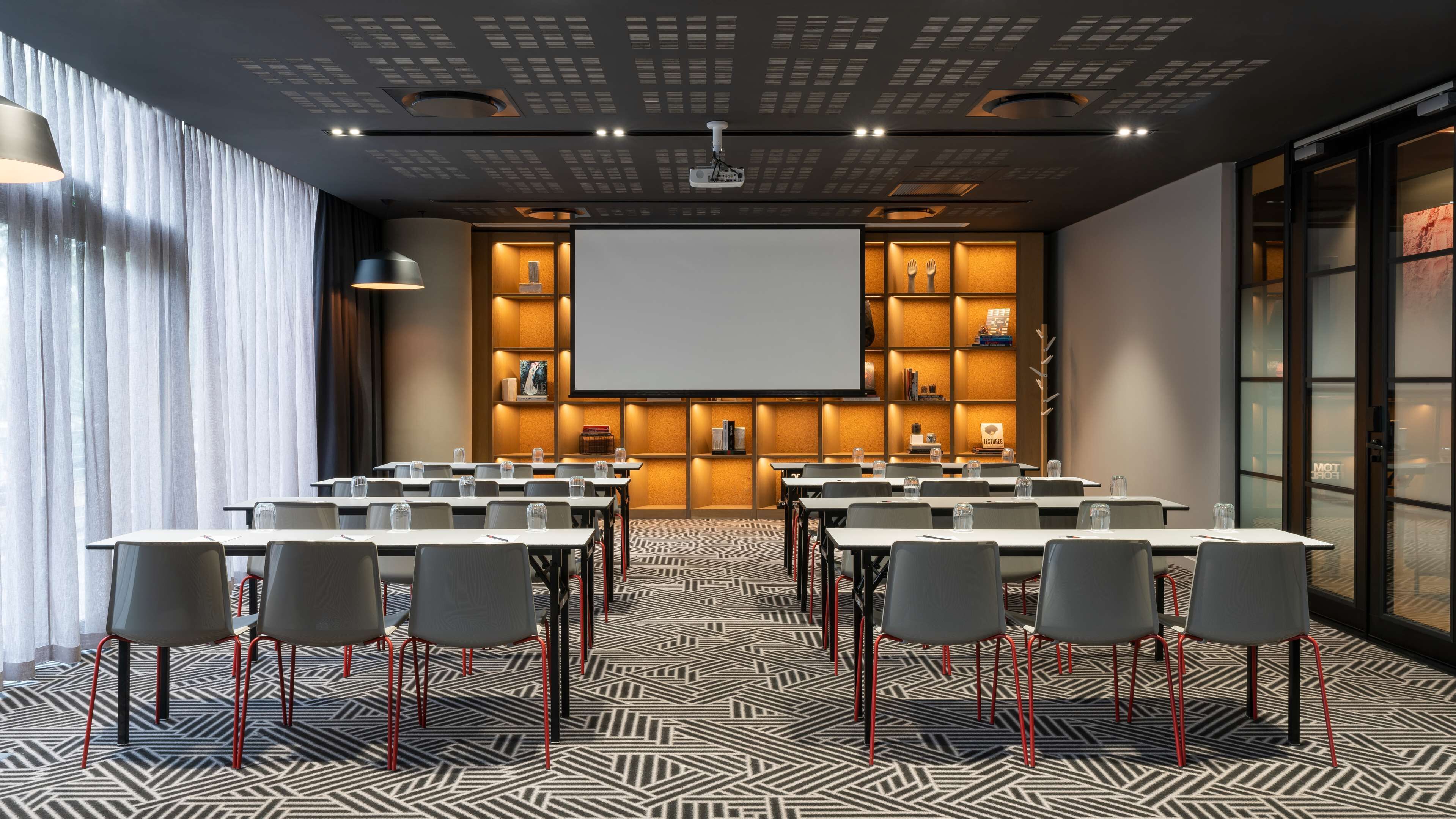 A conference room with a large screen, tables, chairs, and a patterned carpet.