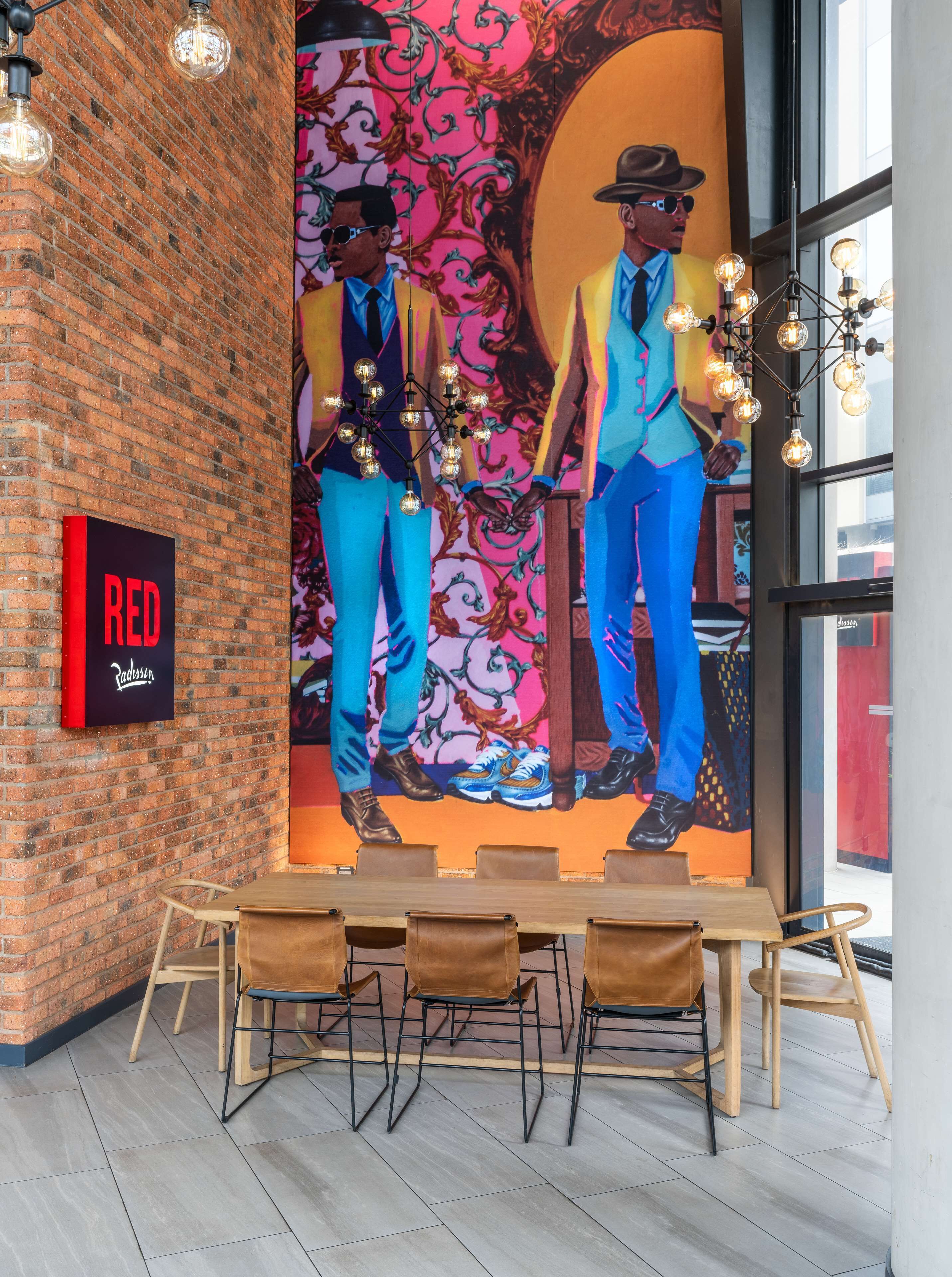 Interior de restaurante com parede de tijolos, um mural de dois homens de terno e uma placa indicando "RED Radisson".