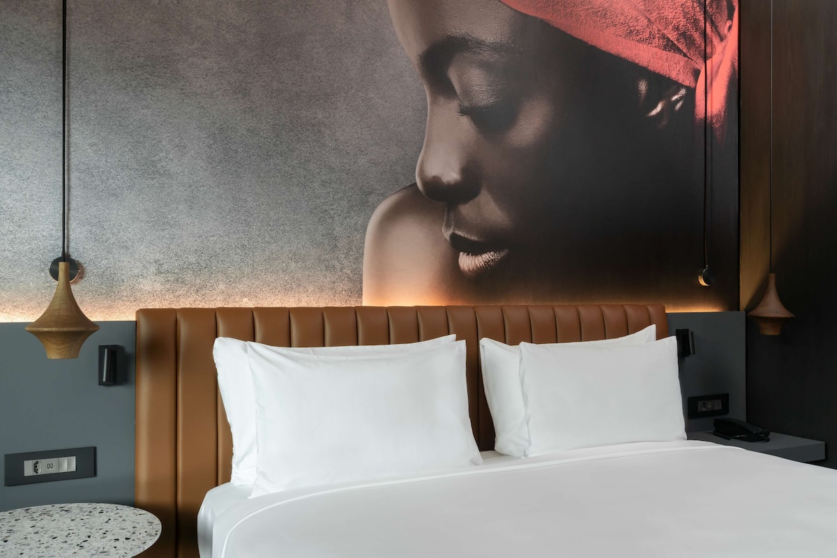 Una habitación de hotel con una cama, una mesa redonda y una lámpara de pared.