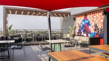 Un espacio al aire libre con mesas y sillas, un mural en la pared y vistas de la ciudad.