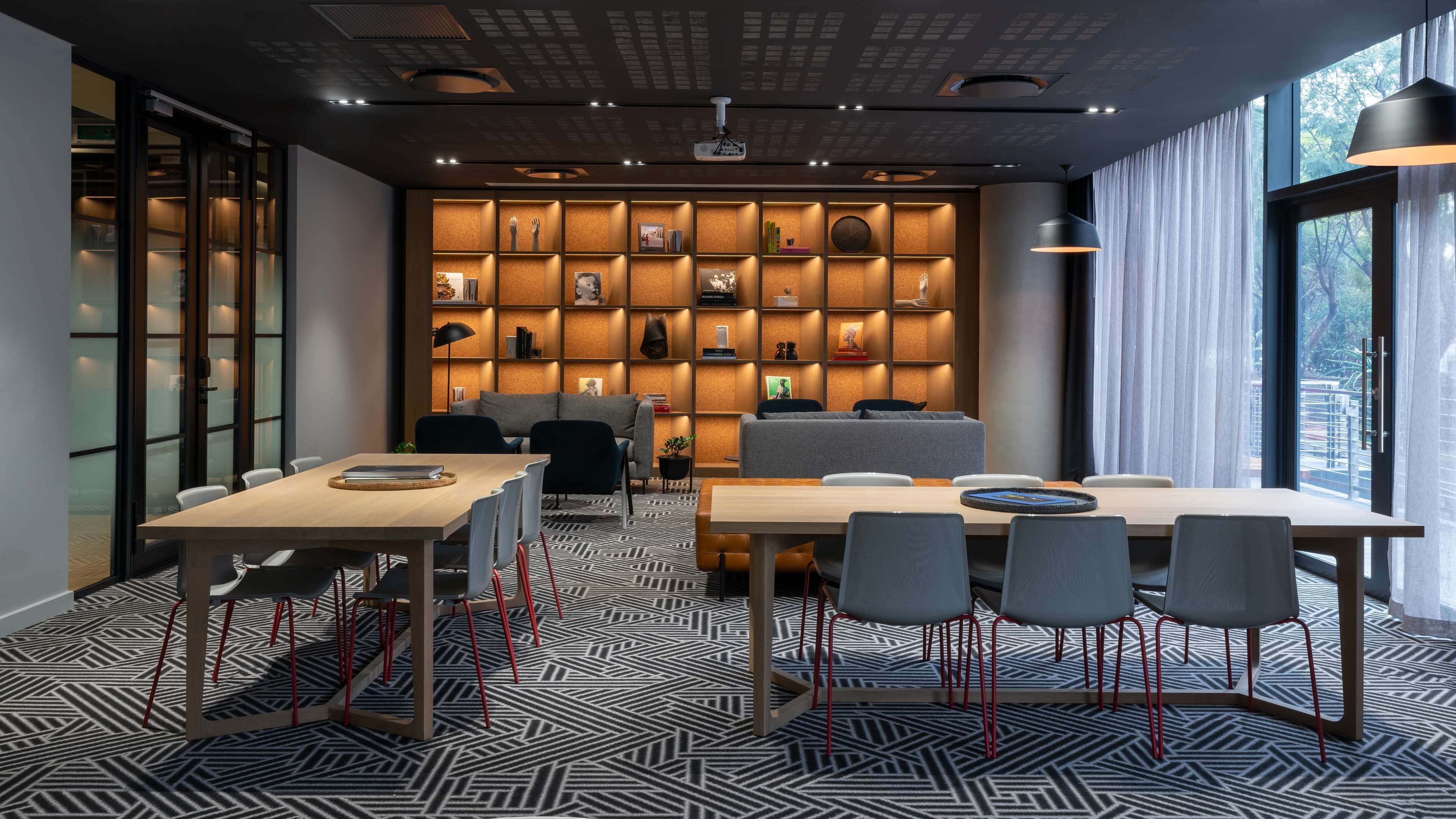 A modern meeting room with a large table, chairs, a sofa, and a bookshelf filled with books and decorative items.